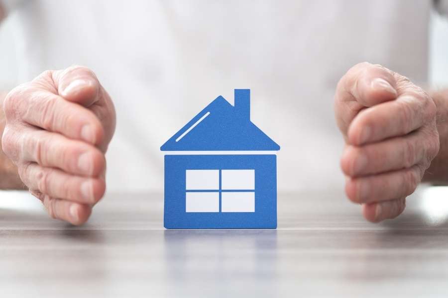 Des mains protégeant une petite maison bleue, symbolisant le choix de la meilleure assurance habitation.