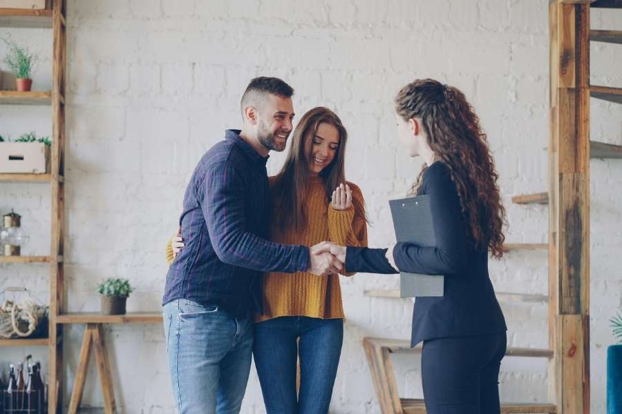 Un jeune couple serre la main d'une agente immobilière après avoir signé des documents pour leur nouveau logement.